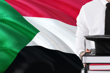 Successful Sudanese student education concept. Holding books and graduation cap over Sudan flag...