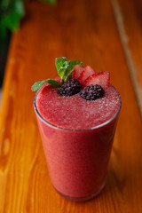 Red smoothie decorated with berries and mint on a table