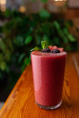 Red smoothie decorated with berries and mint on a table
