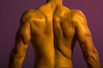 Fototapeta premium back view of shirtless athletic man with muscular torso on purple background