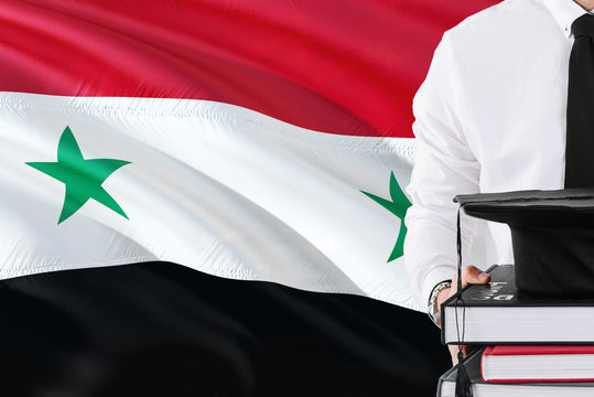 Successful Syrian Student Education Concept. Holding Books And Graduation Cap Over Syria Flag Background.