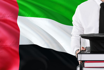 Successful student education concept. Holding books and graduation cap over United Arab Emirates flag background.