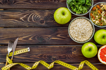 Weight loss concept with oatmeal, nuts, greenery, fruits and measuring tape on wooden background top view copy space