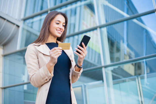 Woman shopping with credit card. Beautiful young lady with gold card using phone