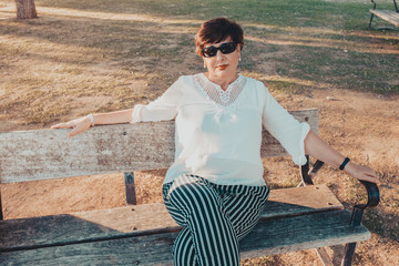 lovely hispanic middle aged woman in the park sitting on a bench at sunset