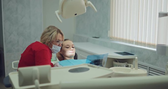 Beautiful female dentist looking at an x-ray picture with a patient. Young girl at the reception at the orthodontist.