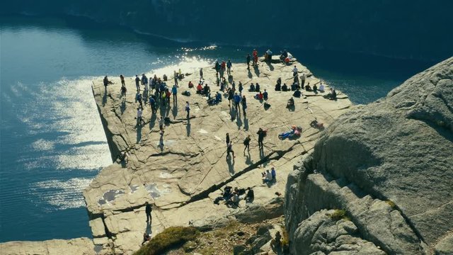 People taking turns on top of Pulpit Rock to pose for pictures, taking up hero positions and standing precariously close to the edge of 604 meters deep abyss above the Lysefjord, mass tourism concept