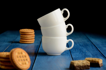 Three white coffee cups, cookies on a blue wooden background.