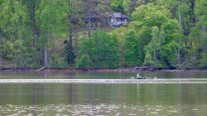 Man in crew boat on lake rowing with trees in the background