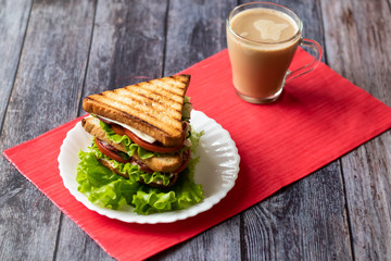 Sandwich with cheese, tomato, cucumber, sausage and salad on wooden background. Coffee with milk Horizontal orientation