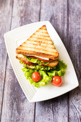 Sandwich with cheese, tomato, cucumber, sausage and lettuce on a wooden background. Vertical orientation