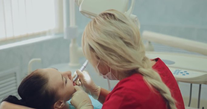 Female dentist drills a tooth to a patient for further treatment. Dentist holds a drill in his hands and gently begins to drill a tooth.