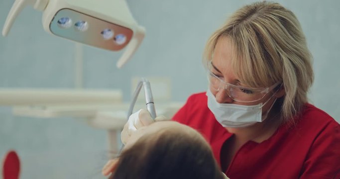Pretty middle-aged woman treats a tooth girl. Dentist drills a tooth to a patient in a modern dental office. Portrait view.