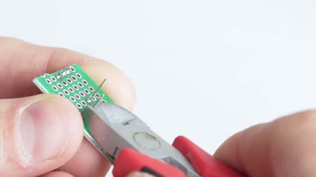 Close up of male person cutting wires of at veroboard soldered electric component with a pair of pliers. White background.