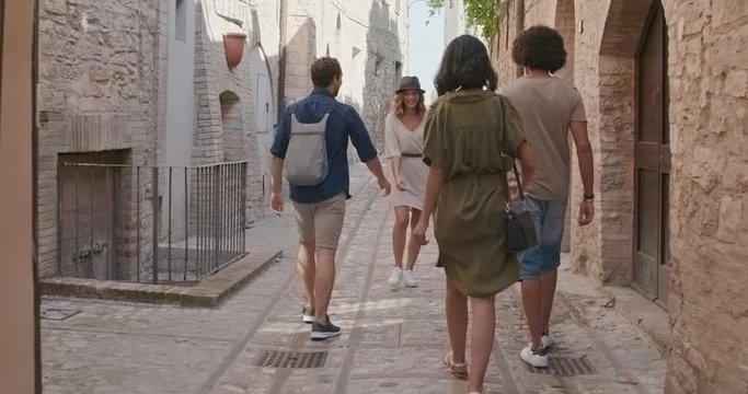 Four happy tourist people walking through small street visiting rural town of Spello.Back follow.Friends italian trip in Umbria.4k slow motion