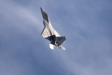 F-22 Raptor in beautiful light against clouds, with the jet stream visible behind the aircraft