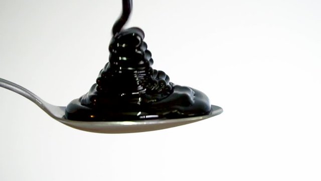 Molasses fills spoon and overflows, slow motion close up