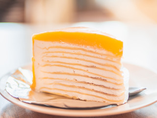 Closeup Orange Crepe Cake on white plate in cafeteria. Selective focus at thin layers of cake.