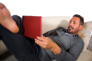 natural lifestyle portrait of young handsome and successful self employed man working at home using laptop computer lying relaxed at living couch networking