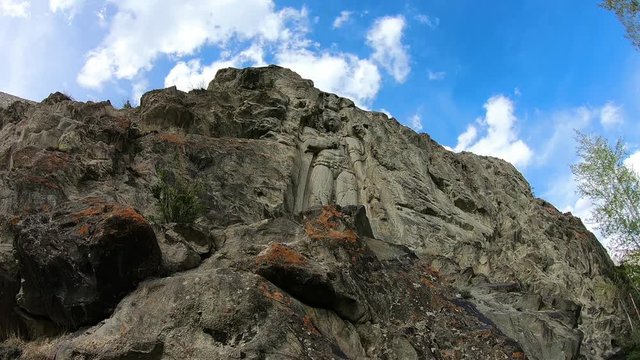 Steady, exterior, time-lapse, medium wide shot of a sculpture of a person carved onto the face of a cliff. Blue sky and clouds quickly moving in background.