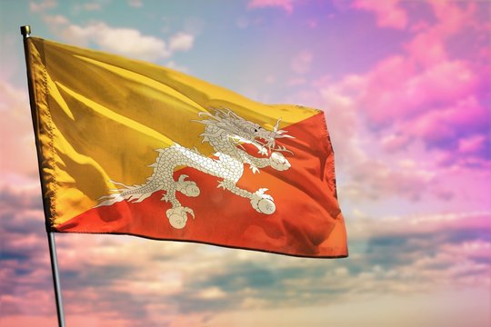 Fluttering Bhutan flag on colorful cloudy sky background. Prosperity concept.