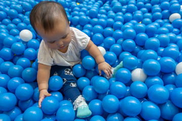 Fototapeta na wymiar Happy Asian baby girl playing in a big dry pond full with blue plastic balls