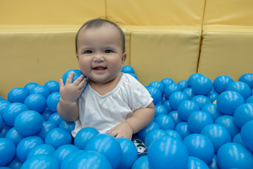 Obraz premium Happy Asian baby girl playing in a big dry pond full with blue plastic balls