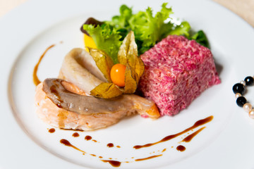Restaurant dish of fish and beet salad in a white plate in the interior close-up.