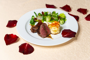 Restaurant dish of pieces of fried meat with a side dish on the table with rose petals.