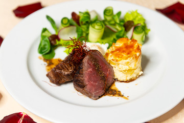 Restaurant dish of pieces of fried meat with a side dish on the table with rose petals close-up.