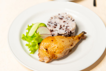 Fried chicken drumstick with rice and vegetables in a white plate on the table. Restaurant menu.