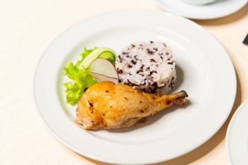 Fried chicken drumstick with rice and vegetables in a white plate on the table close-up. Restaurant menu.