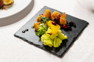 Restaurant dish cheese in batter on a black square plate in the interior.