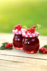 Homemade jam.Red currant jam in a glass jar set on a wooden table in the  rays of the sun on green blurred background. Summer berry jam. Canned berries. Healthy vegetarian sweets