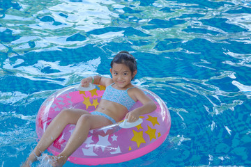 Asian Girl (9-10) sitting on pink inflatable ring in swimming pool, summer vacation concept