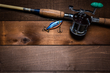 A vintage fishing rod and reel, with a lure on a wooden plank background with copy space