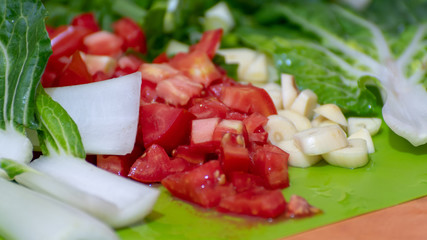 Chef recipe preparation for cooking vegetarian meal. Raw tomatoes, pak choi/ bok choy and garlic vegetable ingredients cut and sliced on kitchen chopping board ready to cook. Healthy vegan stir fry.