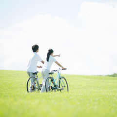 草原で自転車を押すカップルの後姿