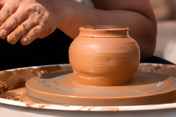 Fototapeta na wymiar Hands of a street potter make a clay pot on a potter's wheel. Close-up