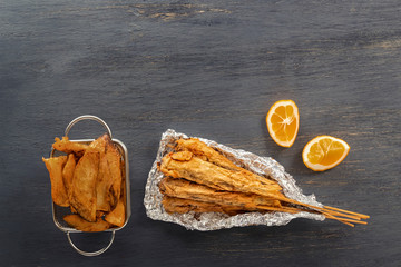 Small fish on skewers baked in foil, lemon and french fries on a wooden table. Copy space