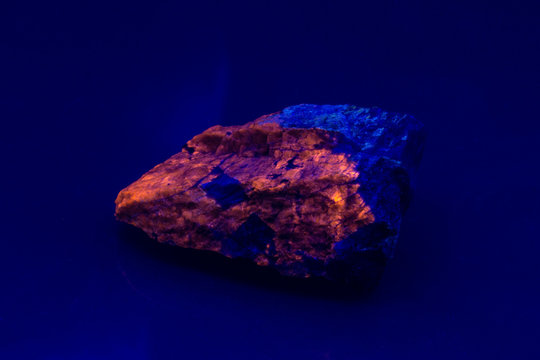 Hackmannite fluorescent mineral under UV light. Luminescent orange crystals in ultraviolet lightening. Hackmannite is a member of the sodalite group of minerals.