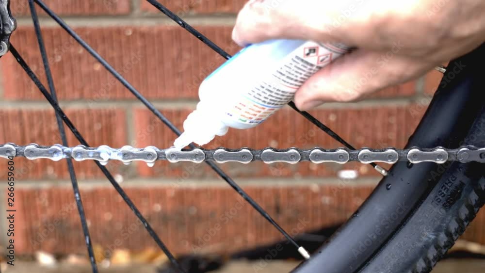 Poster close up of a mechanic placing lubricant on a freshly cleaned bicycle chain as a part of routine mai