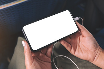 Mockup image of woman's hand holding a black smart phone with blank desktop screen and earphone in...