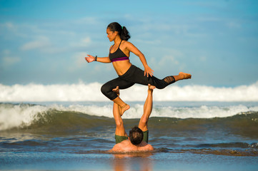 young attractive and concentrated couple of acrobats practicing acro yoga balance and meditation exercise on beautiful beach under a blue sky in mind and body control