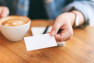 A woman holding and giving a blank empty business card to someone while drinking coffee