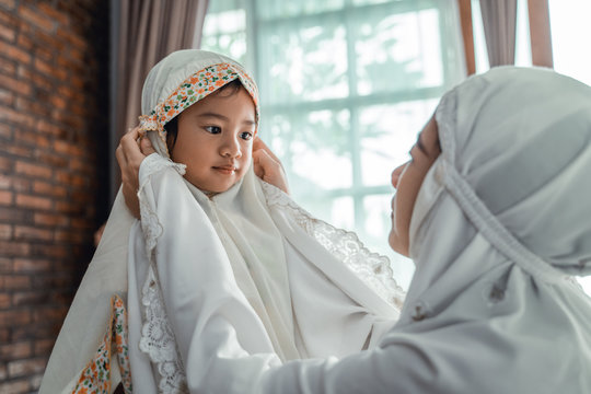 Muslim mother helps young daughter put on scarf before prayer