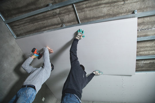 Workers fitting panel into frame of ceiling.