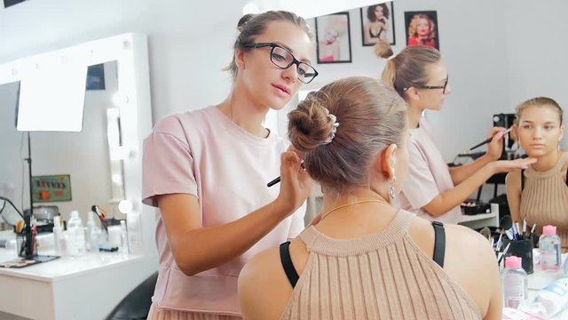 Closeup slow motion video of female visagiste applying makeup on models face in professional makeup studio