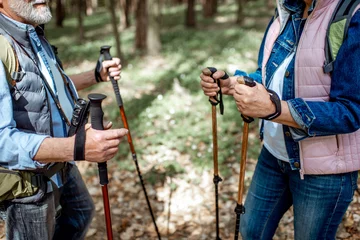 Tuinposter Senior man and woman hiking with trekking sticks in the forest, close-up view with cropped face © rh2010