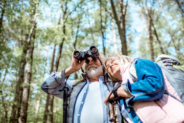 Senior couple looking with binoculars while hiking in the forest. Concept of an active lifestyle on retirement - Powered by Adobe